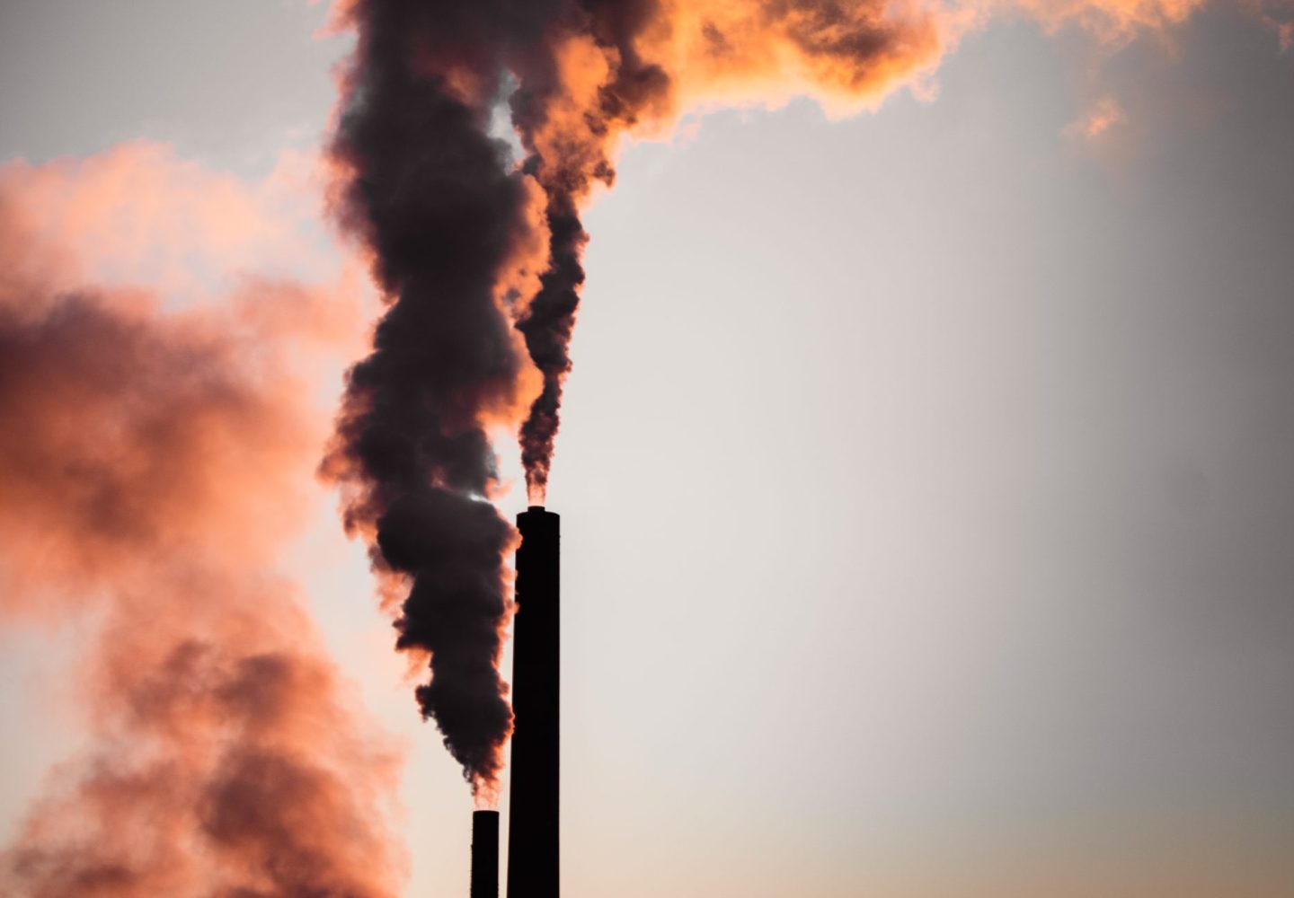 A scenic view of dark smoke coming out from pipes in an industrial plant at sunset